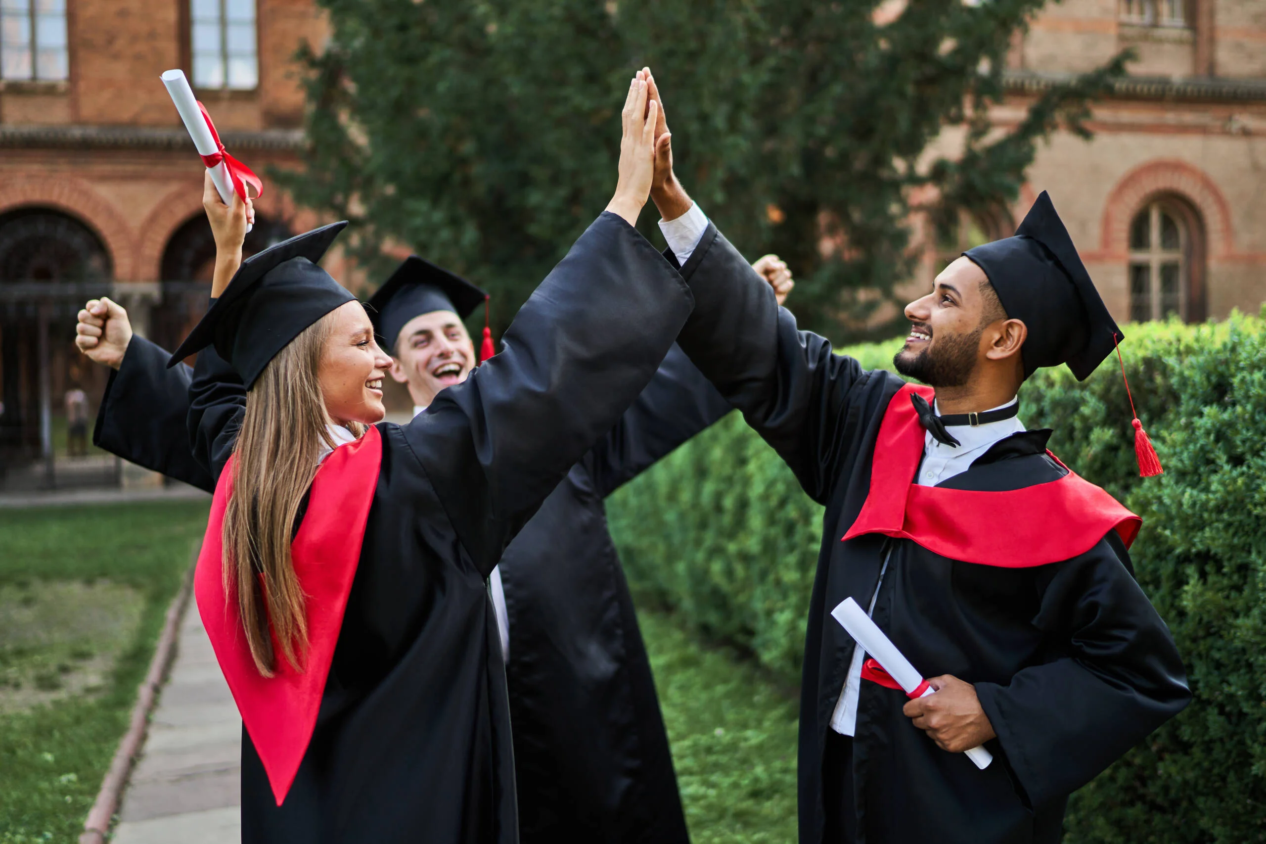 three-happy-international-graduate-friends-greeting-university-campus-graduation-robes-with-diploma-scaled.jpg